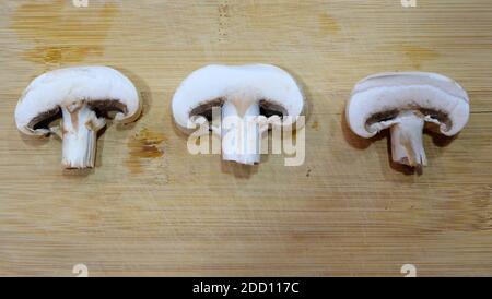 Flay legen von 3 Scheiben geschnittenen weißen Champignons, Seite an Seite auf einer hölzernen Schneidebrett-Oberfläche angeordnet. Stockfoto