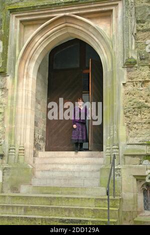 Sie Engländerin, 36 Jahre alt, oben auf den Stufen, vor dem Eingang des Glockenturms der Kathedrale. Inklusive Torbogen und Stufen. Chichester, West Sussex, England. P Stockfoto
