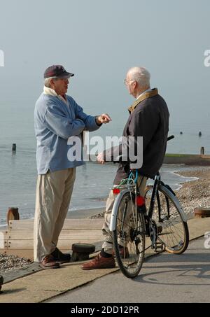 Zwei Männer, mittleren Alters bis ältere, stehen auf Küstenweg in East Wittering, in der Nähe von Chichester, West Sussex reden. Februar. Modellversion. Stockfoto