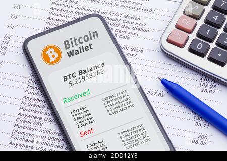 Smartphone mit Bitcoin Wallet auf Kontoauszug mit Rechner und Stift. Stockfoto