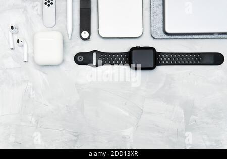 Moderne Alltagsgeräte tragen auf einem konkreten Schreibtisch: Smartphone, Smartwatch, digitales Tablet, Stylus Bleistift, kabellose Kopfhörer, Memory Stick. Schwarz und w Stockfoto