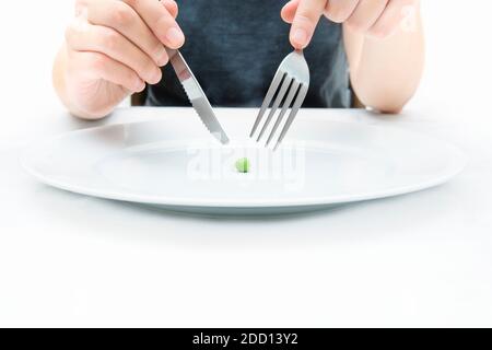 Frau, die eine kleine grüne Erbse mit Messer und Gabel isst. Extreme Gewichtsverlust Diät-Konzept. Stockfoto