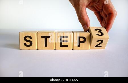 Schritt für Schritt. Zeit bis Schritt 3. Hand dreht einen Würfel und ändert den Ausdruck 'step 2' in 'step 3'. Schöner weißer Hintergrund. Geschäft und nächster Schritt CO Stockfoto