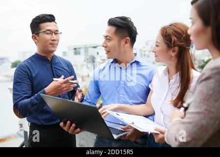 Gruppe von jungen asiatischen Geschäftsleuten diskutieren Präsentation auf Laptop Angezeigt Stockfoto