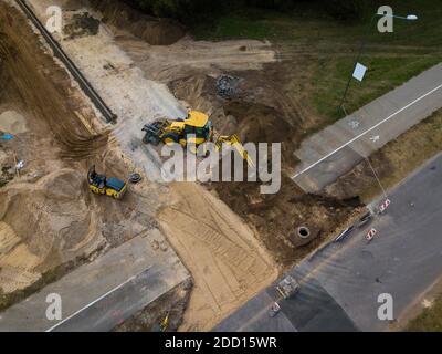 Blick von oben auf Straßenbauarbeiten. Schwere Ausrüstung. Riesiger Bagger und Straßenwalze. Schwarz und Weiß. Stockfoto