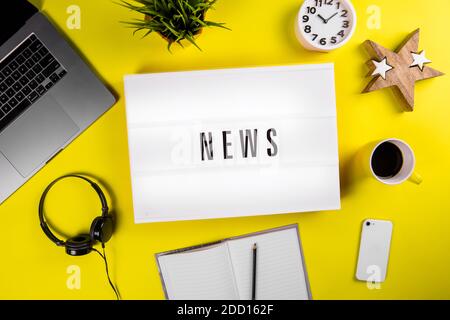 News Wort auf Leuchtkasten auf modernen gelben Büro-Desktop mit Laptop, Smartphone Stockfoto
