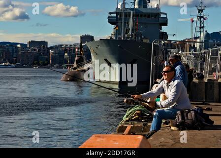 Oslo, Norwegen - 29. August 2020: Angler Angeln im Hafen durch festmachen Kriegsschiffe und U-Boot. Stockfoto