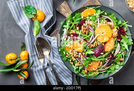 Frischer hausgemachter Mandarine- und Rübensalat mit Rucola, Walnüssen und Pinienkernen auf grauem Betongrund. Gesundes veganes Essen. Draufsicht. Stockfoto