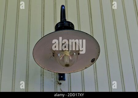 Alte weiße und schwarze Wandleuchte aus einer Metallscheibe, mit einer Glaskuppel, die die Glühbirne schützt. Stockfoto