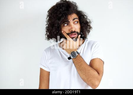Entschlossener arabischer Mann mit Bart denkt und schaut besorgt, steht vor weißem Hintergrund. Stockfoto