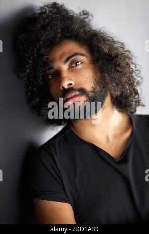 Nahaufnahme Porträt von lockigen indischen Mann mit tiefen Blick, gutaussehende Kerl in lässigen schwarzen T-Shirt ist in der Kontemplation Stockfoto