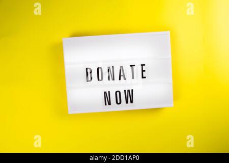 Jetzt spenden Text auf Leuchtkasten auf gelbem Hintergrund isoliert Draufsicht, flach liegend Stockfoto