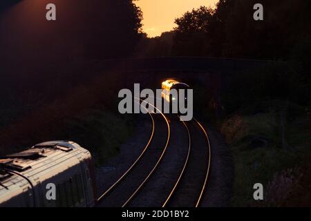 Transport für Wales Klasse 158 Dieselzug 158818 mit einem Goldglint bei Sonnenuntergang vorbei an einem anderen Zug in Cheshire Stockfoto