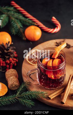Heißer Glühwein in Glas Tasse auf dunklem Hintergrund. Warmes Weihnachtsgetränk mit Gewürzen und Früchten. Stockfoto
