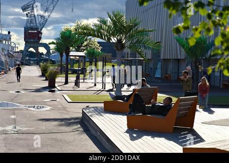 Oslo, Norwegen - 29. August. 2020: Menschen entspannen in einem öffentlichen Park an den Docks, Park ist mit Bänken und gefälschten Kunststoff Palmen geschmückt. Stockfoto