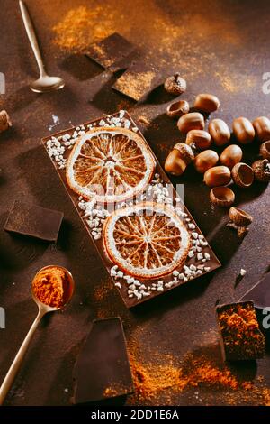 Kandierte Orangenscheiben in Schokolade liegen auf einem dunkelbraunen Hintergrund, neben Besteck. Schieferhintergrund. Stockfoto