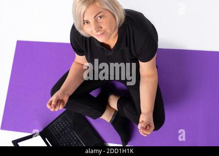 Ältere Frau sitzt vor dem Laptop und schaut auf die Kamera. Foto von oben. Stockfoto