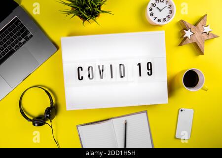 COVID 19 Wort auf Leuchtkasten auf modernen gelben Büro-Desktop Globale Quarantäne Stockfoto