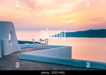 Weiße Architektur auf Santorini Insel, Griechenland. Restaurant im Freien unter einer fantastischen Sonnenuntergangslandschaft, Stühle für Paare. Romantischer Blick auf den Sonnenuntergang Stockfoto