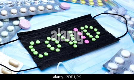 Die Aufschrift COVID aus grünen und rosa Pillen auf dem Hintergrund einer schwarzen Maske, Flatlay Stockfoto