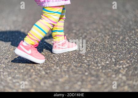 04.12.19 - Provence, Frankreich: Süße kleine Mädchenbeine mit Nike rosa Sportschuhen und Regenbogenhosen. Niedliche Foto im Freien von Mädchen spielen. Stockfoto