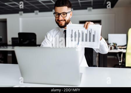 Ein junger Mann, der auf einer Webkonferenz mit Kollegen über eine Laptop-Webcam spricht, ein männlicher Mitarbeiter, der mit Kollegen per Videoanruf spricht Stockfoto