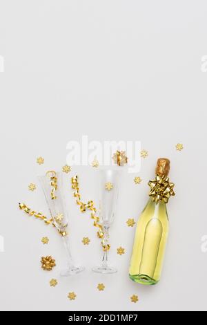 Festlicher weißer Hintergrund mit Golddeko, Flasche Sekt mit zwei Kristallgläsern, glänzend goldenen Serpentin Konfetti und Schneeflocken Stockfoto