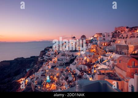 Atemberaubende Sonnenuntergangslandschaft. Schöne Aussicht auf fabelhafte Dorf Oia mit traditionellen weißen Häusern und Windmühlen in Santorini Insel bei Nacht, Griechenland Stockfoto