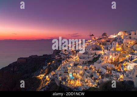 Atemberaubende Sonnenuntergangslandschaft. Schöne Aussicht auf fabelhafte Dorf Oia mit traditionellen weißen Häusern und Windmühlen in Santorini Insel bei Nacht, Griechenland Stockfoto