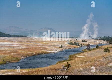 Der Firehole River fließt durch das Midway Geyser Basin, Yellowstone National Park, Wyoming. Dampf steigt aus dem Excelsior Geyser und Grand Prismati Stockfoto