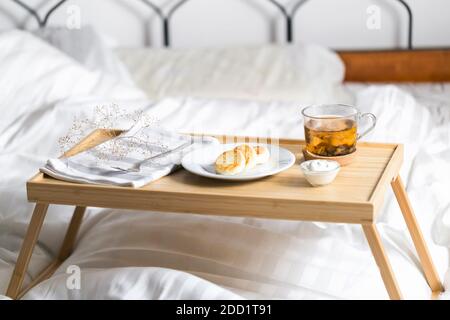 Gelbe Hüttenkäse Pfannkuchen auf dem Bett Tablett Tisch mit Schwarzer Tee und saure Sahne und Serviette am Morgen Stockfoto