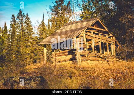Eine alte Hütte auf dem Land befindet sich in einem Zustand des Verderbens, wobei das Schindeldach in einen Rahmen mit fehlenden Brettern einsackt. Stockfoto
