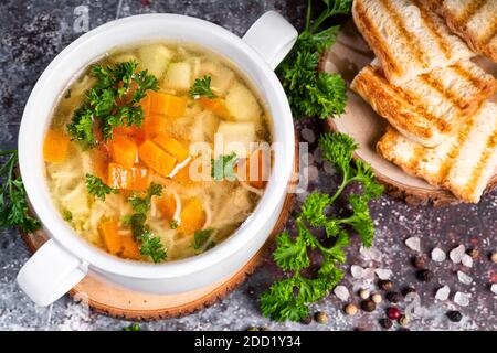 Ein Teller Suppe mit Gemüse und Kräutern mit Brot Toast auf dunklem Hintergrund Stockfoto