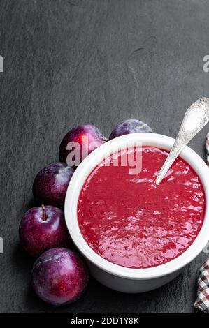 Hausgemachtes Chutney aus Pflaumen in Tonschale auf schwarzem Stein Hintergrund Stockfoto