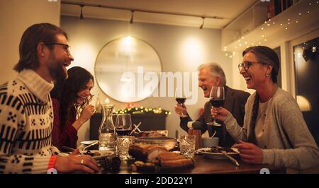 Fröhliche Familie, die am Esstisch sitzt und sich unterhielt und Rotwein trank. Familie mit Weihnachtsessen zu Hause. Stockfoto