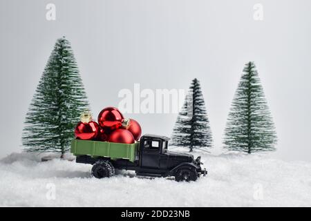 Ein Spielzeugauto fährt durch den Schnee im Hintergrund sind rote Weihnachtskugeln. Stockfoto