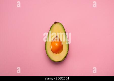Avocado mit Eigelb in der Mitte auf rosa Hintergrund. Kreatives Food-Konzept Stockfoto
