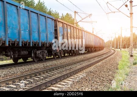 Schwergutfracht Rosty Zug Waggons bewegen sich auf der Eisenbahn bei Sonnenuntergang oder Sonnenaufgang Tageszeit. Transportkonzept für Industriematerialien und Warenlieferung Stockfoto