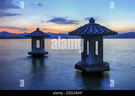 Zwei steinerne Laternen an der Imperial Marina am West Lake in Hangzhou, China auf einem Sonnenuntergangshintergrund. Stockfoto