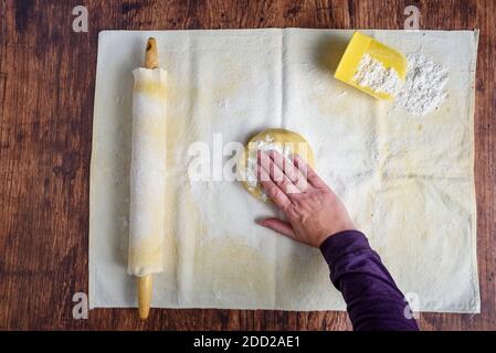 Die Hand der Frau drückt eine Kugel Zuckerkekenteig nach unten Auf einem Backstuch und überzogen hölzernen Nudelholz auf Ein Holztisch Stockfoto