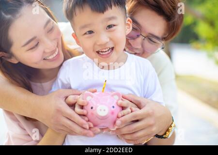 Glückliche Eltern halten Sparschwein und lehren Sohn Geld sparen Stockfoto