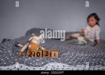 Neujahrskarte. Handgemachtes Spielzeug Stier Ochse sitzt durch Holzwürfel mit den Zahlen 2021. Ein Kind spielt auf einem unscharfen Hintergrund, sitzt auf der Couch Stockfoto