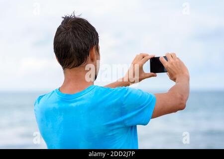Mann fotografiert die Meereslandschaft auf einem Handy Stockfoto