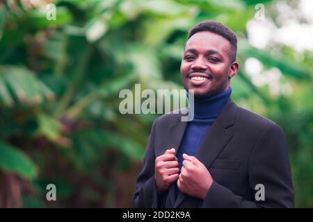 Schöner afrikanischer Geschäftsmann im trendigen formellen schwarzen Anzug. Kerl mit Bart trägt blaue Langarm oder Pullover Stockfoto