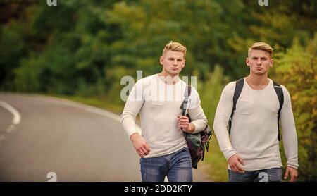 Firmenfreunde Reisende, die auf dem Naturhintergrund der Straße hitchwandern. Beginnen Sie mit dem Wandern ein tolles Abenteuer in Ihrem Leben. Fahren Sie in der Nähe des Stadtrandes. Reisende auf dem Weg. Freunde, die hitchhitchhamps unterwegs Stockfoto