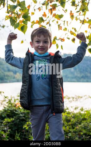 Junge sitzt auf einer Bank in einer medizinischen Maske, Herbstpark Stockfoto