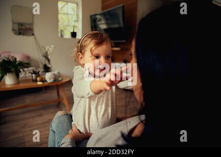 Porträt von niedlichen kleinen Kleinkind Mädchen auf dem Schoß der Mutter sitzen Nase berühren und zu Hause spielen Stockfoto
