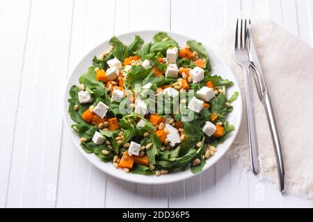 Frischer Salat mit Rucola, Kürbis, Feta-Käse und Pinienkernen auf weißem Tisch. Leckere gesunde Lebensmittel Stockfoto