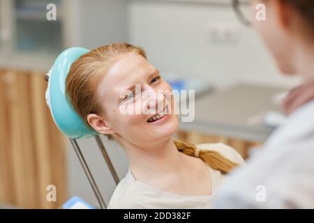 Junge Frau sitzt auf Zahnarztstuhl und lächelt zum Arzt Während ihres Besuchs in der Zahnklinik Stockfoto