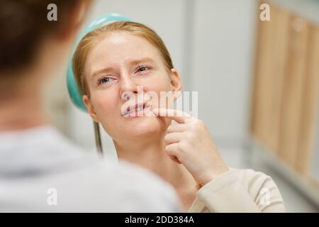 Junge Frau zeigt auf ihr Gesicht und beklagt sich über Zahnschmerzen Zum Zahnarzt während ihres Besuchs Stockfoto